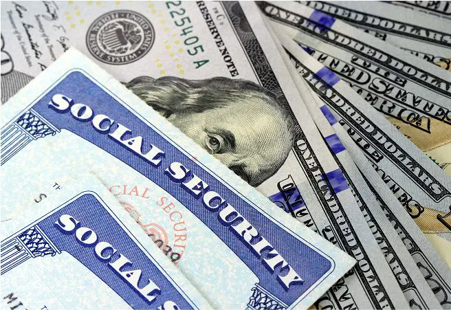 Close-up of Social Security cards placed on top of scattered U.S. dollar bills, including $20 and $50 notes, with the Social Security Administration seal visible.